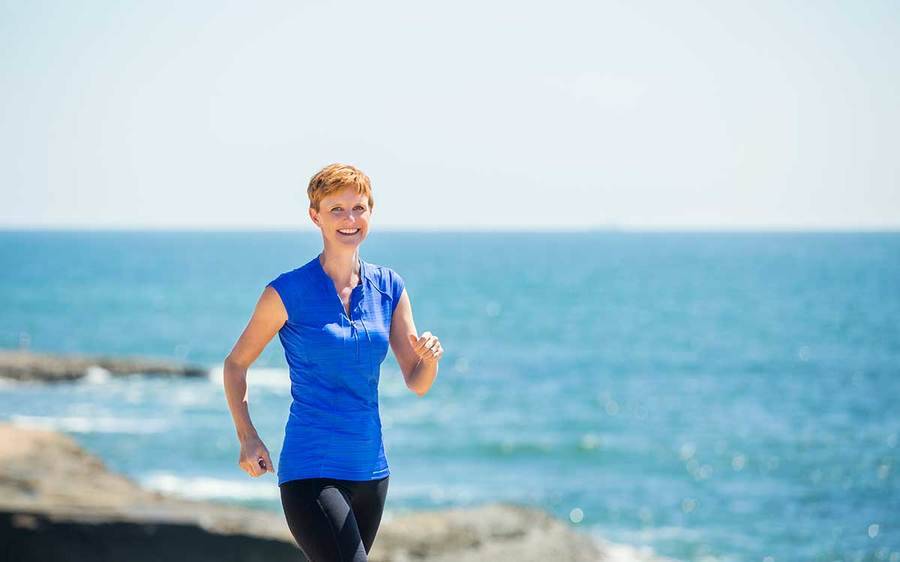 A woman smiling as she is excerising on the coast.