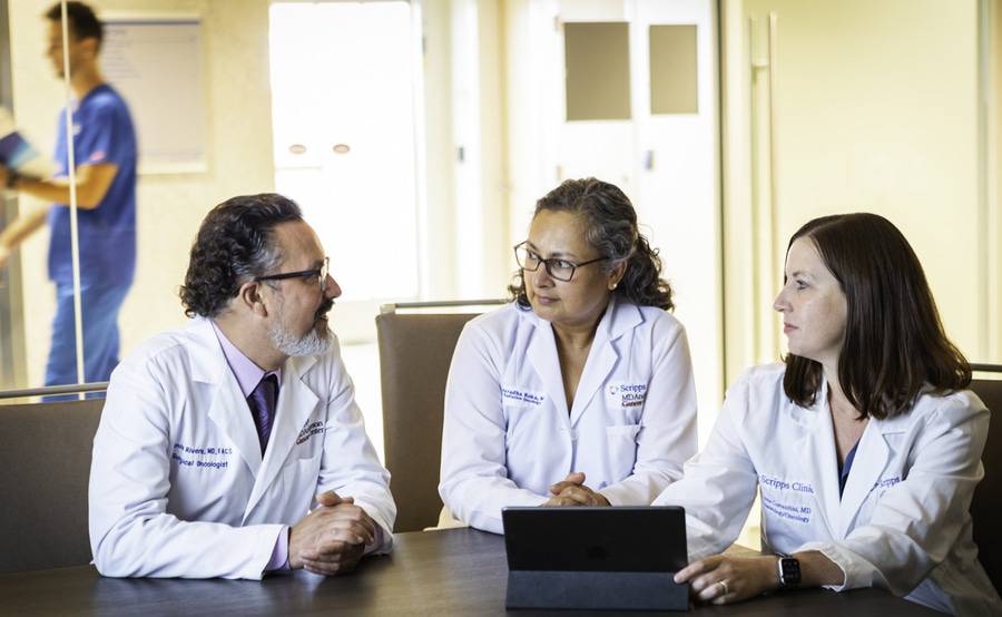 Three Scripps MD Anderson Cancer Center oncologists review incoming physician referrals for cancer patients on a tablet.