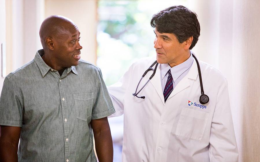 A mature male doctor talks with a black male patient, representing Scripps' commitment to patient experience and safety.