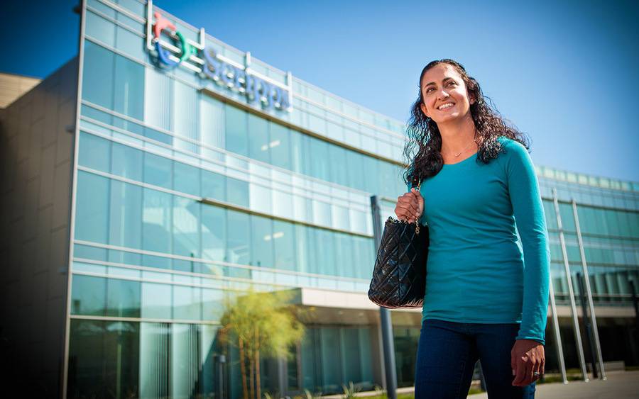 A mature woman in a teal long-sleeved shirt walks near the exterior of a Scripps location, showing why to choose Scripps.