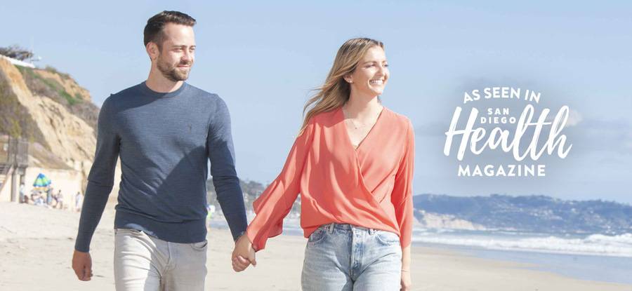 A man and woman hold hands and smile while they walk on the beach - San Diego Health Magazine Fall 2023 issue