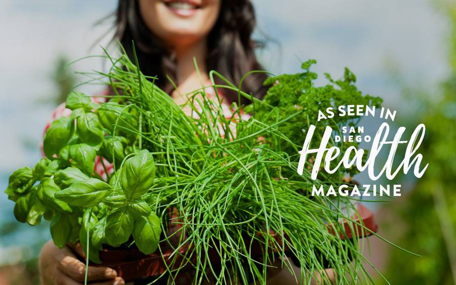 A woman hold a handful of fresh herbs, including basil, chives and parsley.