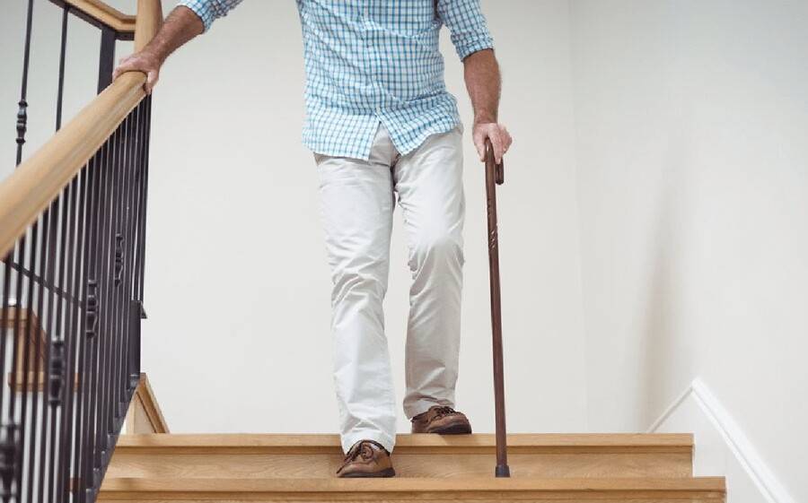 A senior citizen uses handrail to help him walk down stairs with aid of cane.