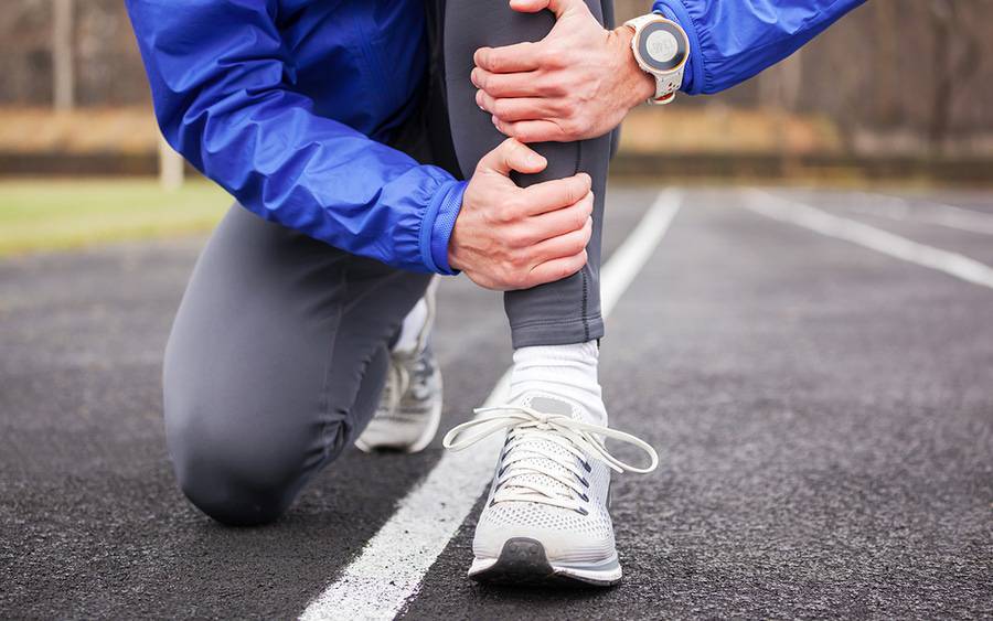 Man knelt on ground grabbing with leg in pain from shin splints.