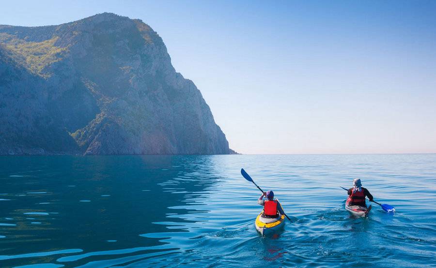 Two people paddle their kayaks around a mountain, representing an actively lifestyle after shoulder surgery.
