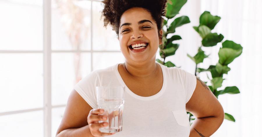 An African American woman laughs while holding a glass of water.