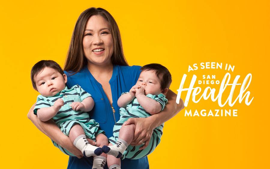 A smiling woman holds her healthy twin baby boys, feeling grateful for the high-risk pregnancy care and neonatal intensive care they received at Scripps.