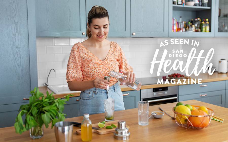 A woman in her kitchen creates a healthier non-alcoholic beverage with sparkling water, lime and oranges. San Diego Health Magazine