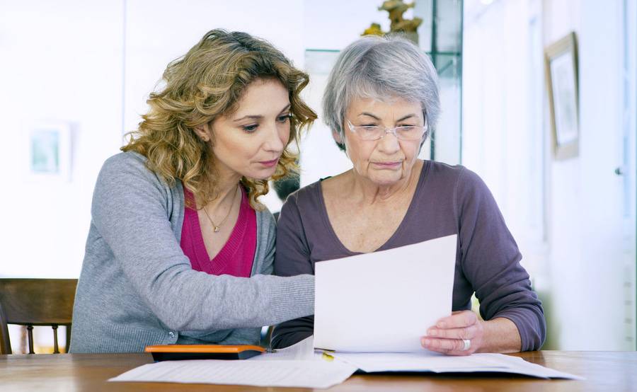 A female social worker helps an older woman review paperwork.