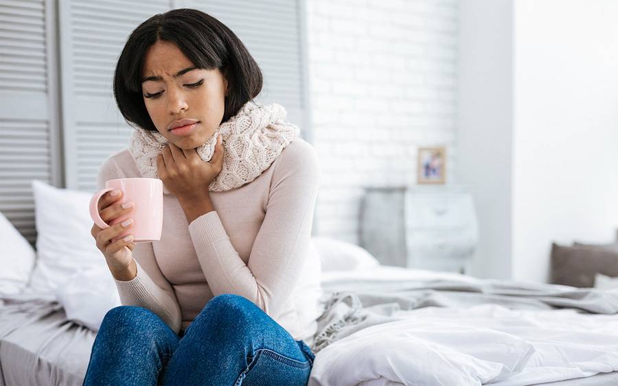 Young woman with sore throat covers her neck and nurses self with liquids.