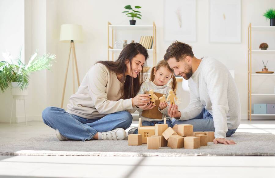 A mother and father playing with their daughter on the floor of a playroom.