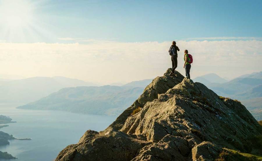Two people stand on a mountain peak, representing an active lifestyle with expert sports medicine.