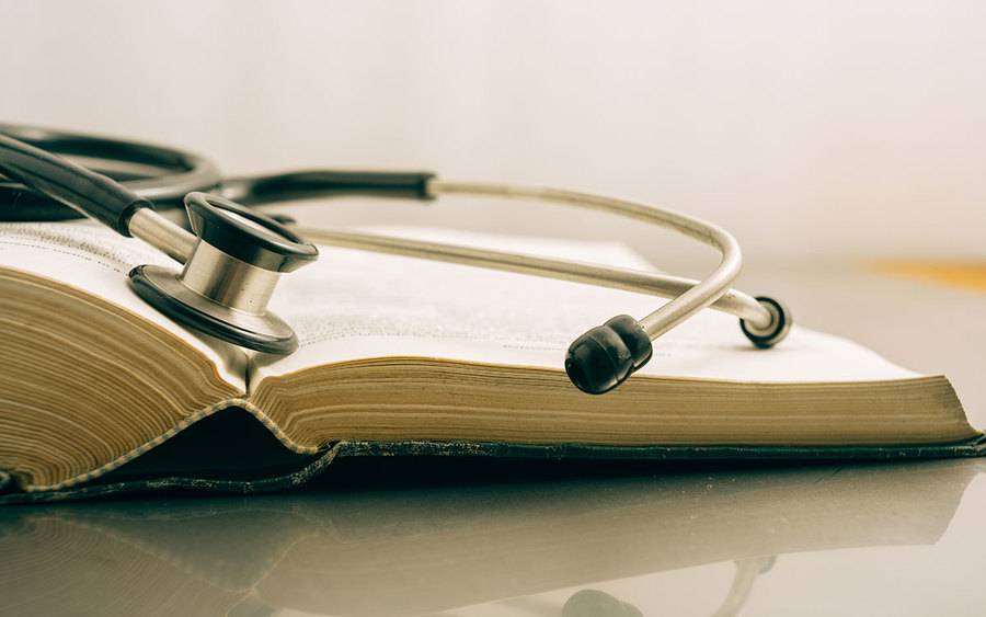 An book is open on a table with a stethoscope on top of it.