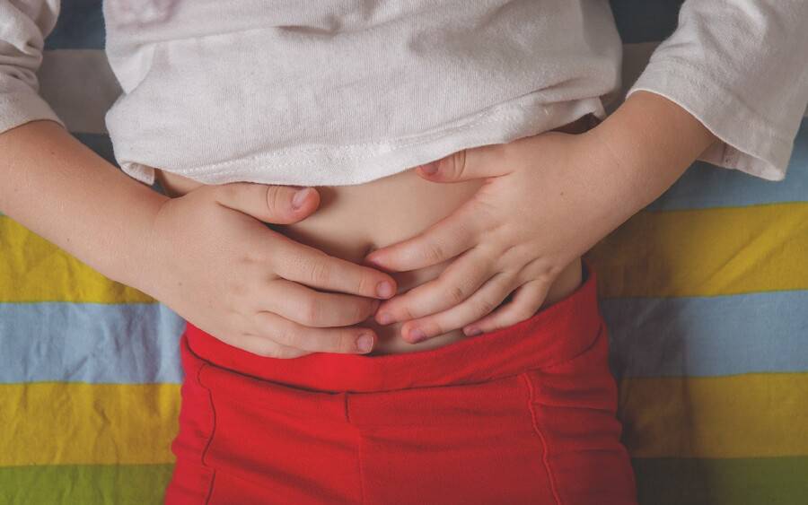 Child with stomachache holding his belly.
