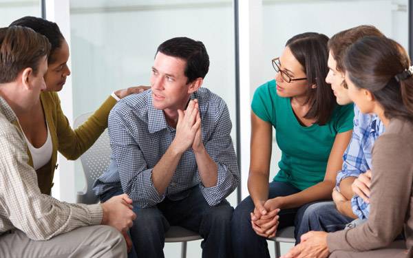 A group of adults comforting and support an individual in the group.