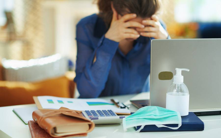 A woman with her head in her hands looking distressed with a face mask and hand sanitizer nearby illustrating COVID anxiety.