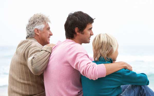 Three generations sit together on the beach, representing a strong support system.