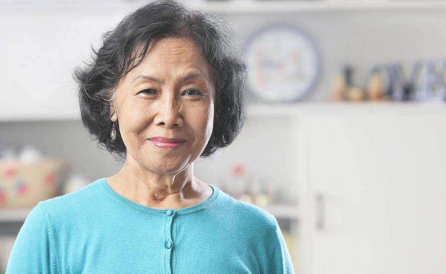 A smiling mature woman in her kitchen represents the importance of knowing the signs and symptoms of stroke.