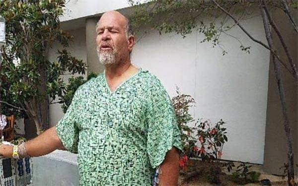 Dennis Baca, a colorectal cancer survivor, stands with his eyes closed beneath a tree.
