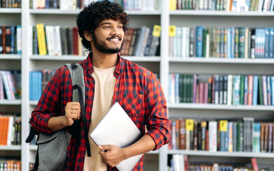 A young healthy looking college freshman smiles in the library surrounded by books.
