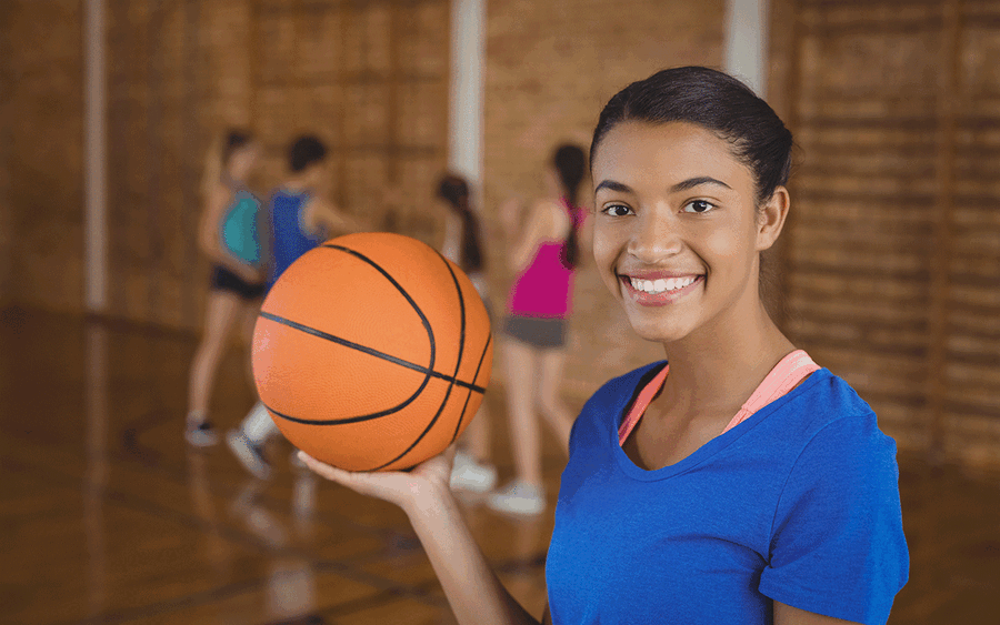 A female teenager in a gymnasium holding a basketball an smiling.