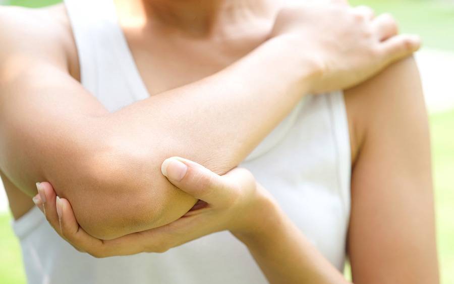 A young woman holds her elbow in pain.