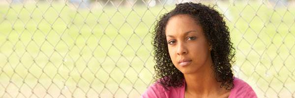 Woman in pink shirt standing in front of softball field.