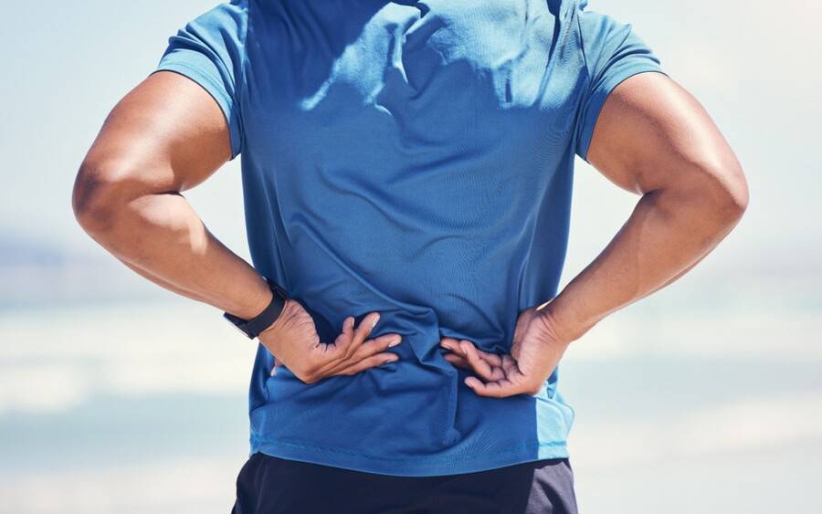 A muscular man grabs his aching back. Did he throw out his back playing sports?