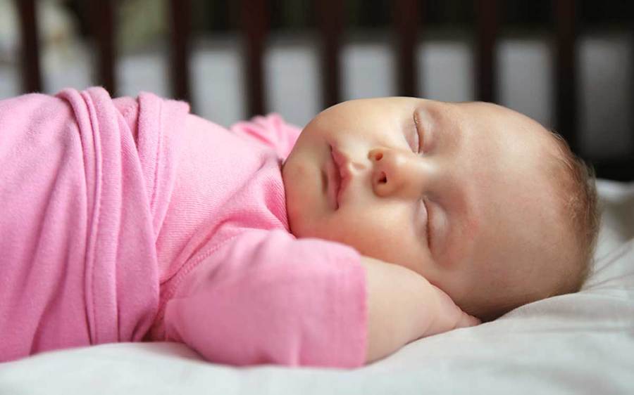 A sleeping baby lies on its back in a pleasant indoor environment.