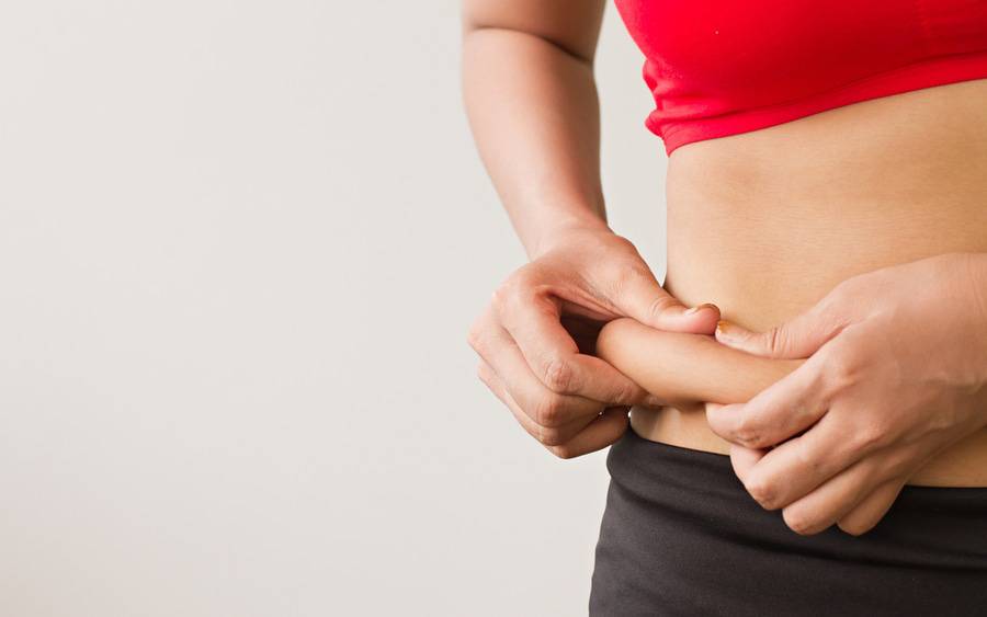 Woman shows belly fat before scheduling a tummy tuck procedure.