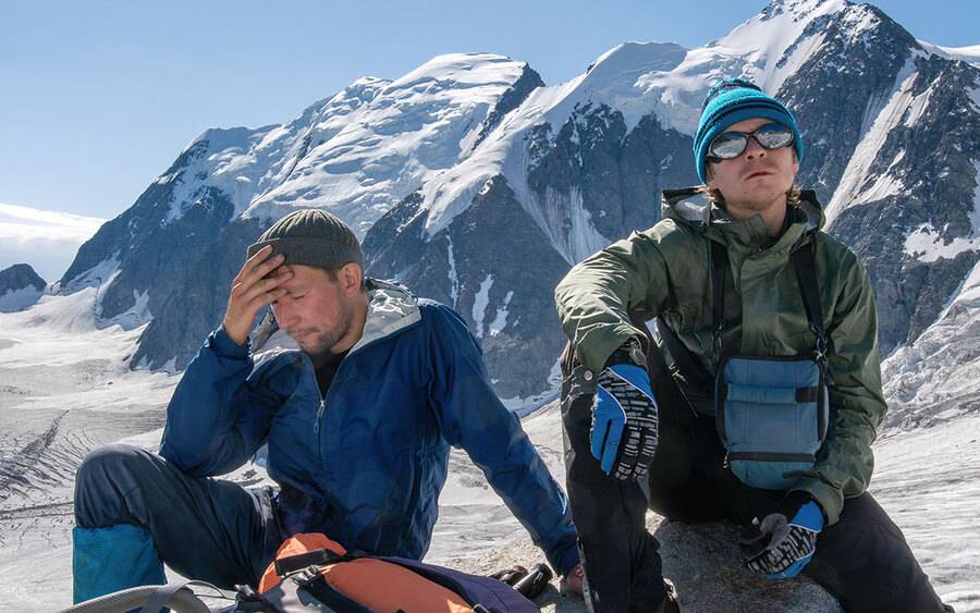 Two men resting on a snowy mountain after climbing the mountains.