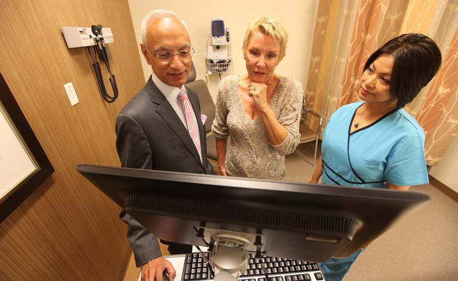 A Scripps radiation oncologist and nurse talk with a mature Caucasian woman in a patient exam room, representing the help patients get in understanding the different types of radiation therapy.