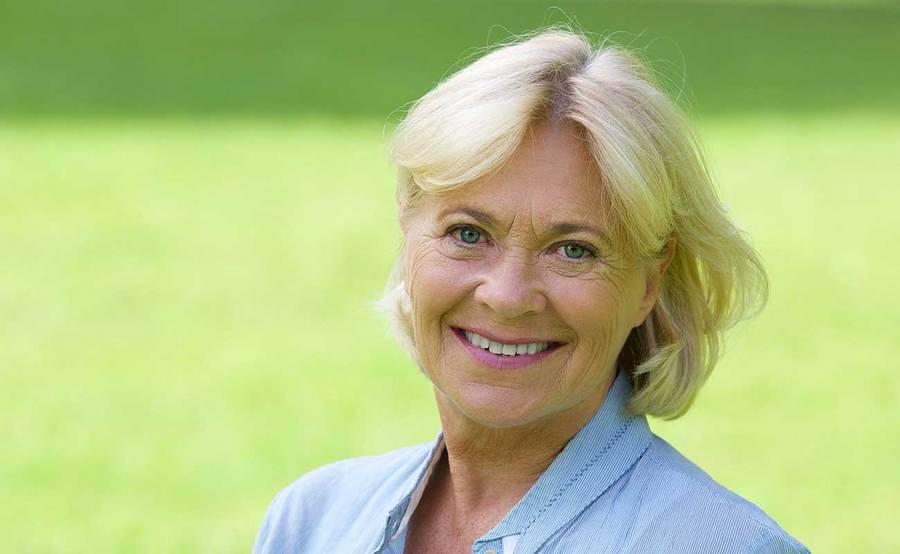 A smiling mature woman in a park represents the full life that can be led after vaginal cancer treatment.