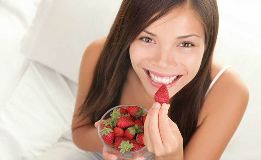 A happy woman prepares to bite into a heart-healthy strawberry.