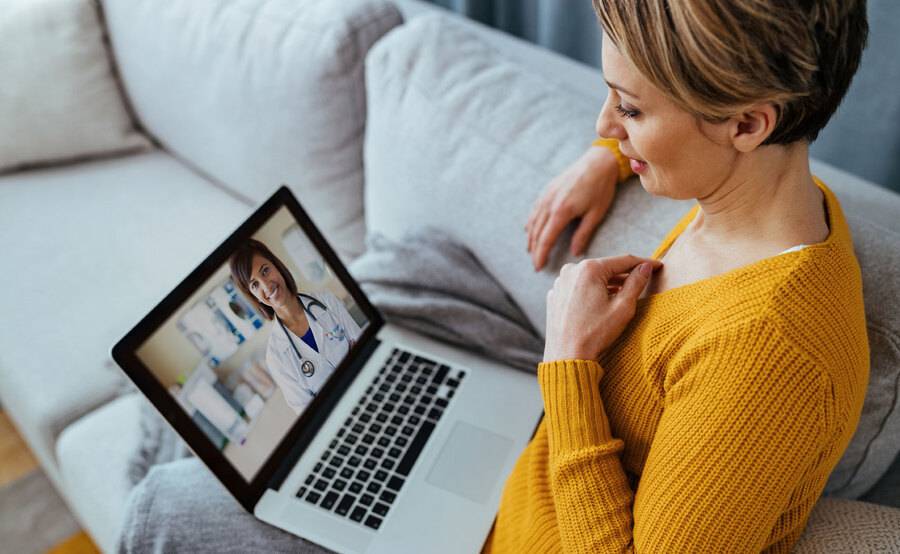 A woman talks with her physician by video on her laptop computer on her couch.
