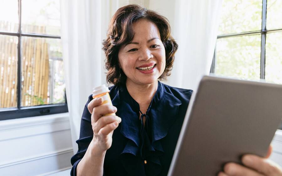 Telemedicine patient using tablet and holding prescription to show her doctor via video.