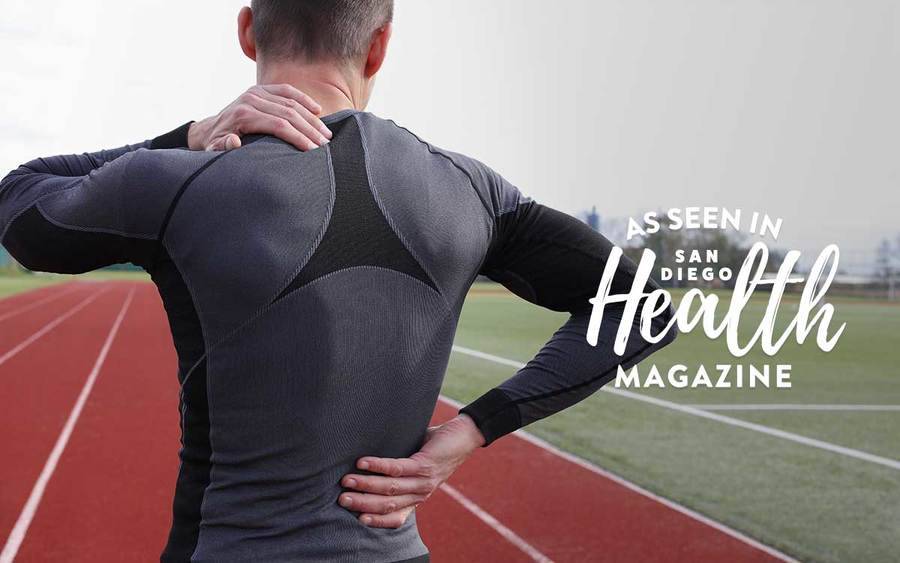 A man working out at a track massages his achy neck and back.
