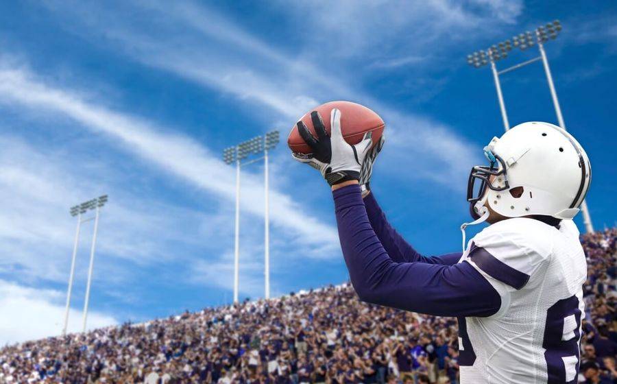 A college football player catches a pass in a packed stadium. Hopefully his vitamin D levels are high enough to avoid injury.