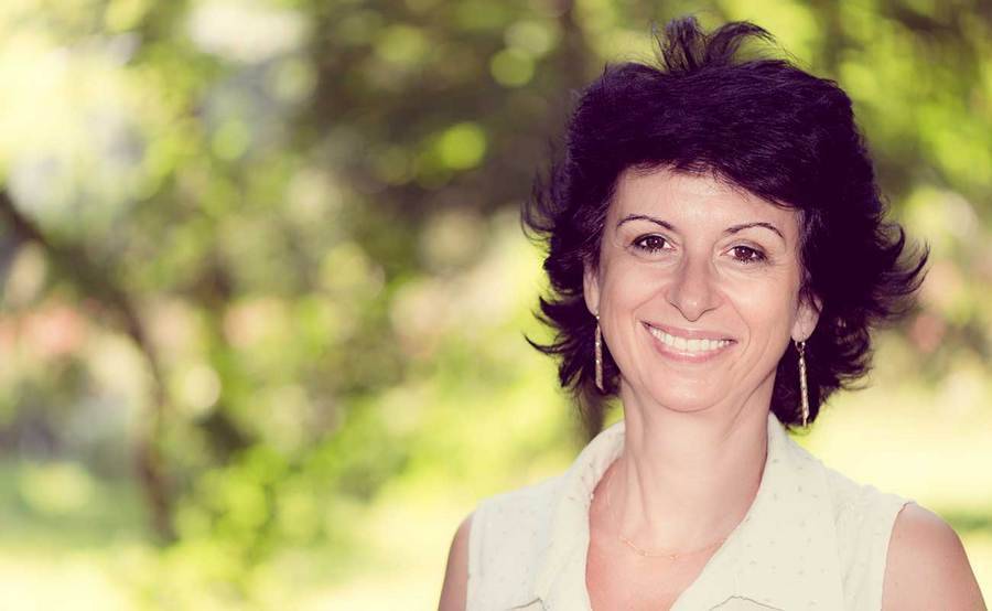 A smiling middle-aged woman in a park represents the full life that can be led after vulvar cancer treatment.