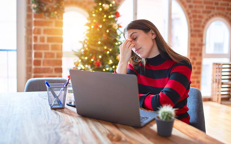 A stressed woman sits in front of her laptop worrying about holiday season demands on her time and finances.