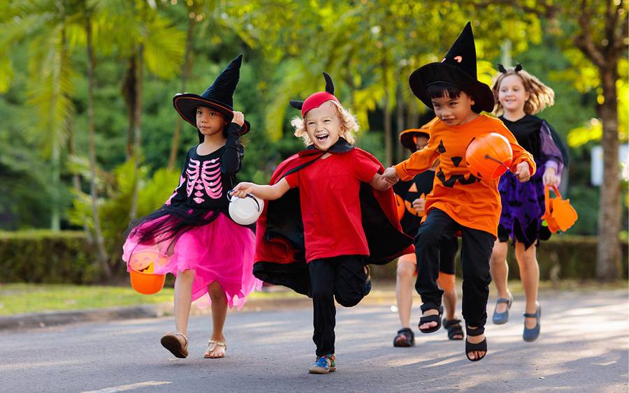 Kids in Halloween costumes skip and run along the streets.