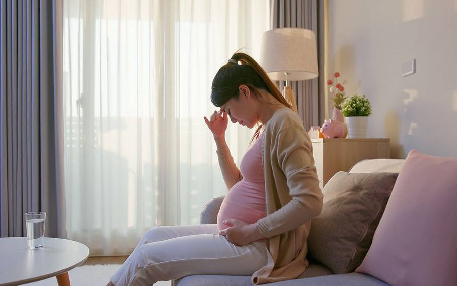 A pregnant woman grabs her head, experiencing morning sickness and other discomforts of pregnancy.