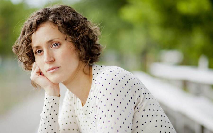 A concerned woman rests on a park bench in an outdoor setting