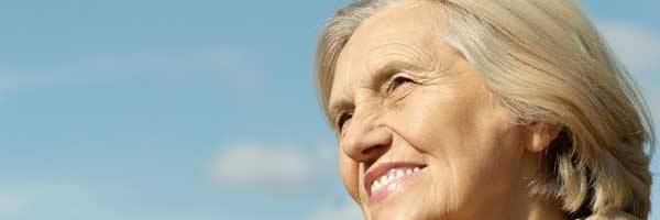 Thoughtful woman in her fifties smiling with blue skies and white clouds in the background.