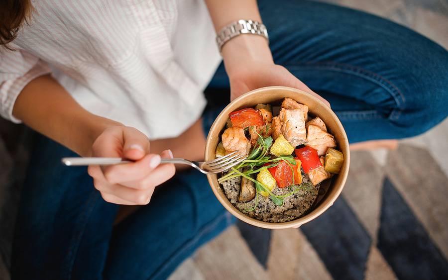 A woman holds a bowl of salmon, vegetables and grains, representing a healthy meal following federal dietary guidelines.