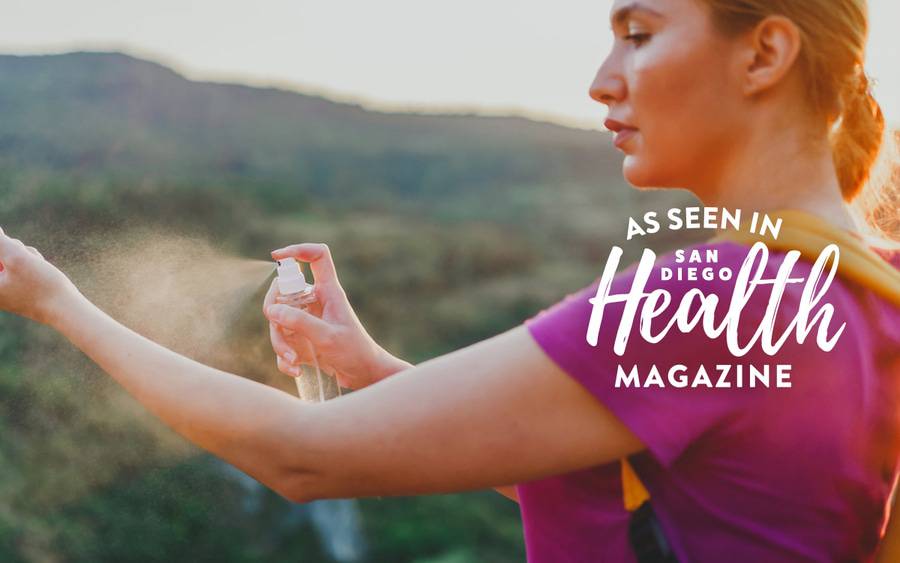 A woman spraying her arm with bug spray to help in preventing bug bites while hiking.