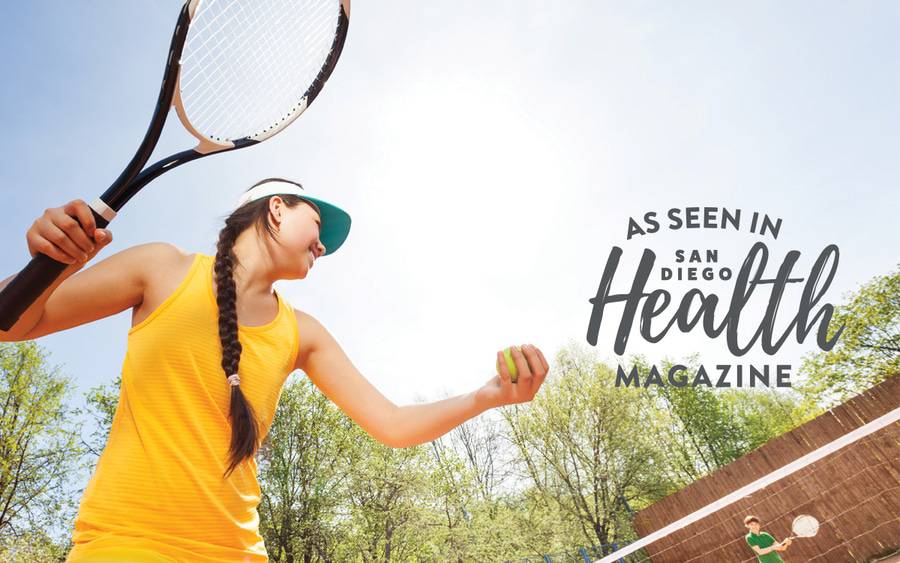 A woman getting ready to serve the ball over the tennis net in the sun.