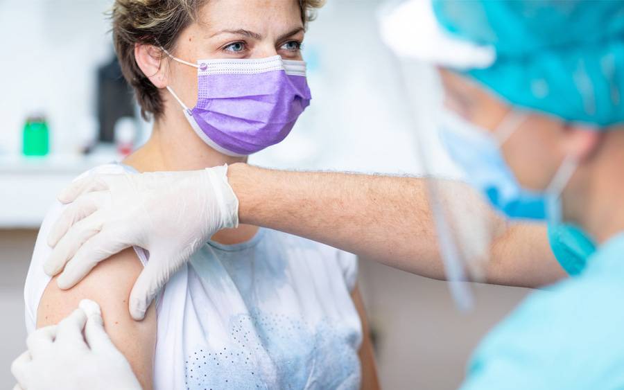 A woman in a mask receiving a flu vaccine at a flu clinic administered by a health care provider in personal protective equipment.