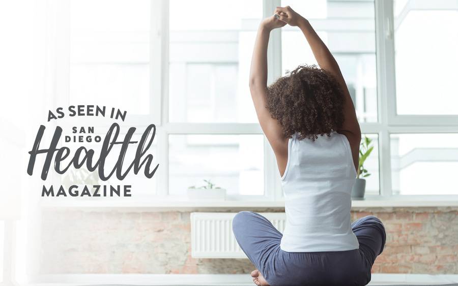 A woman sitting at home stretching her back.