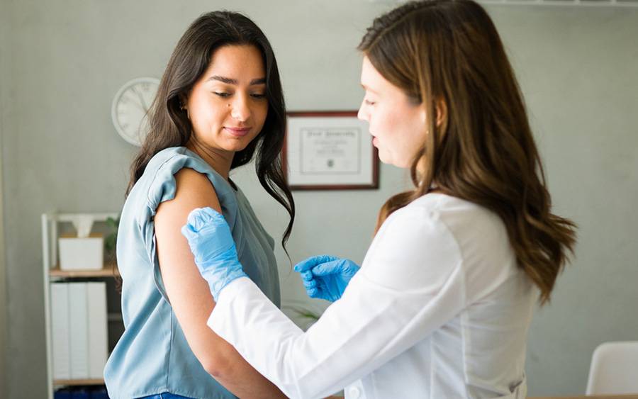 A young woman in her 20s is receiving her annual flu vaccination from a female provider.